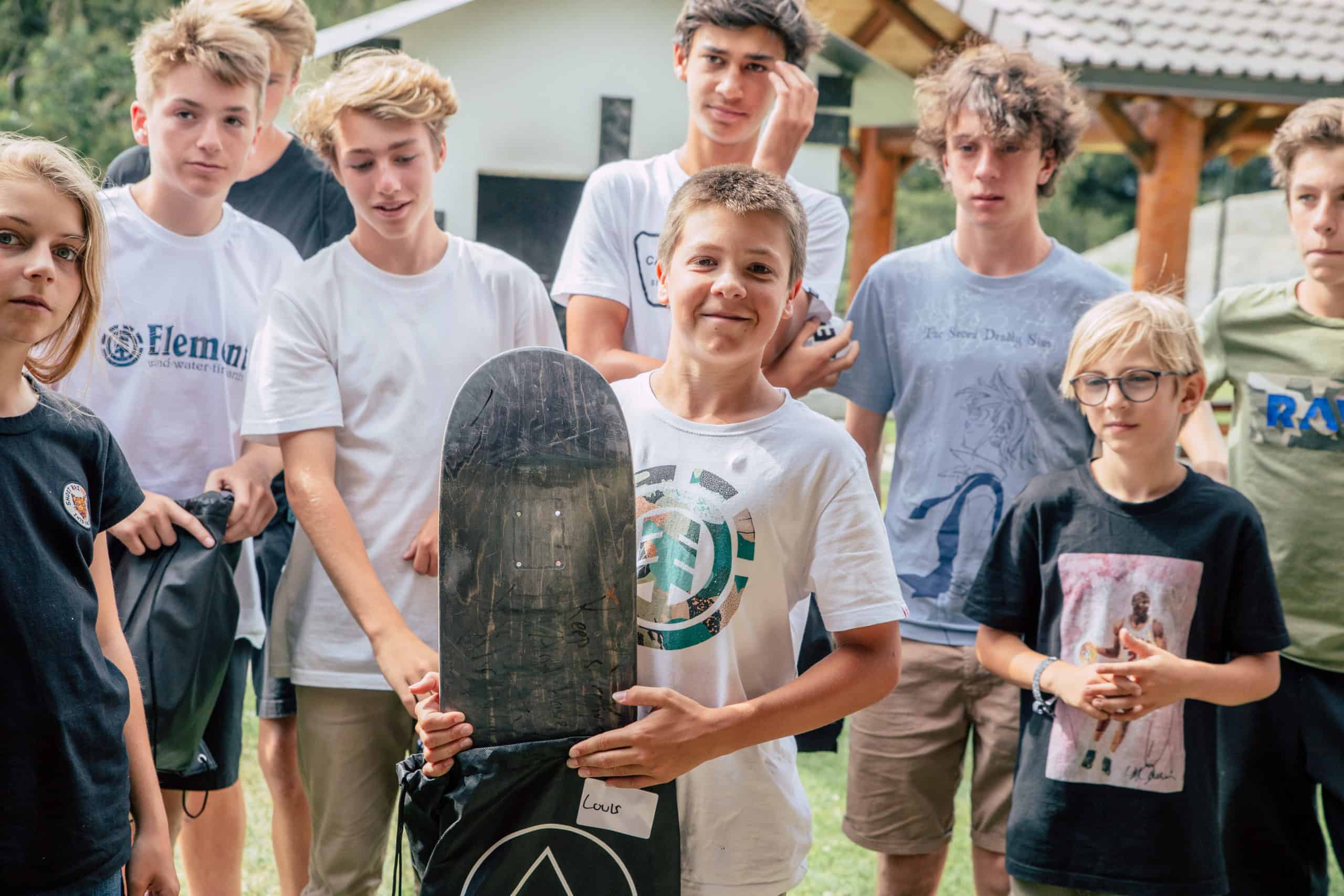 children smiling, one holding a skateboard